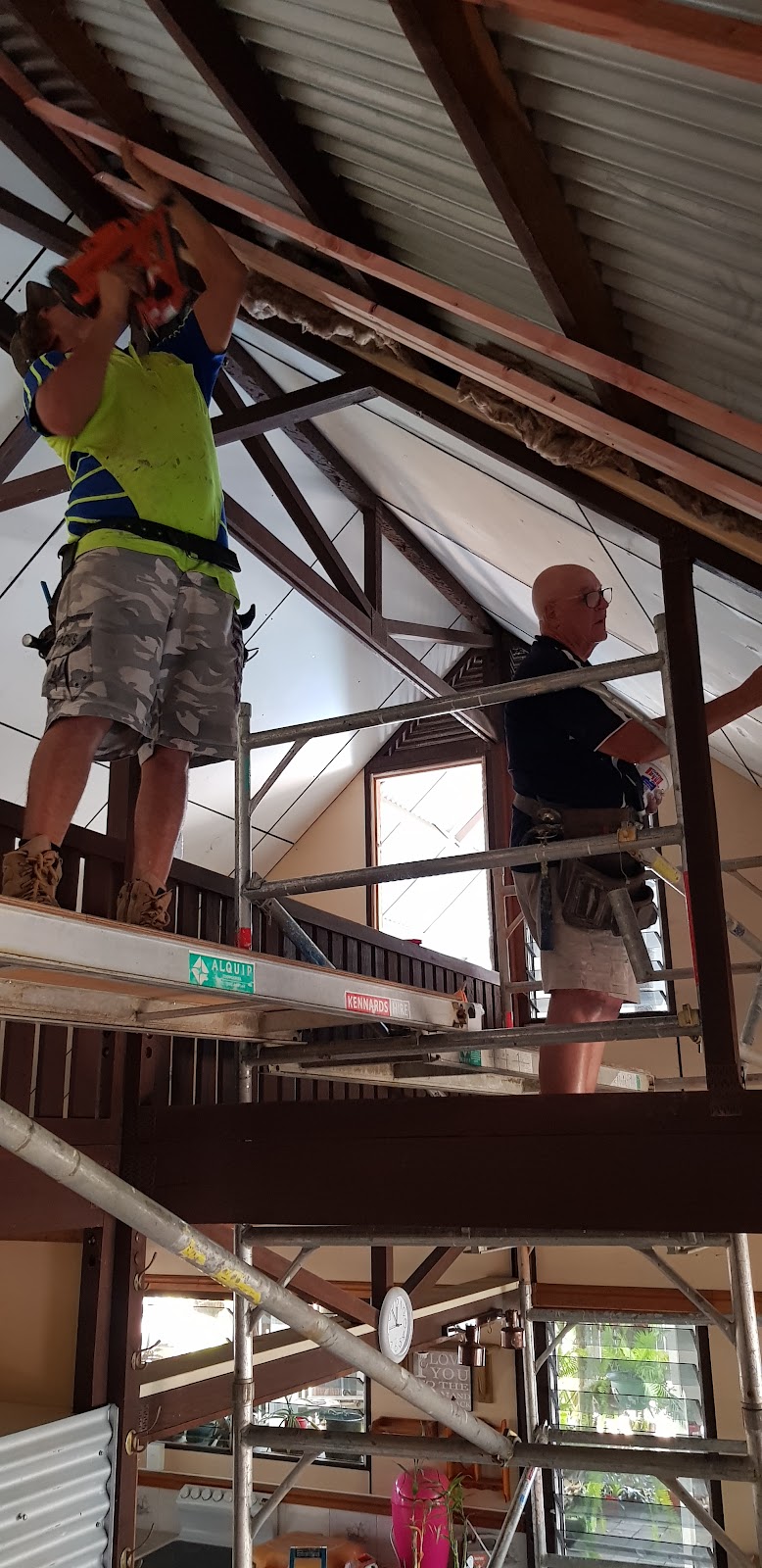 Two tradesmen on mobile scaffolding working under a raked timber-truss ceiling